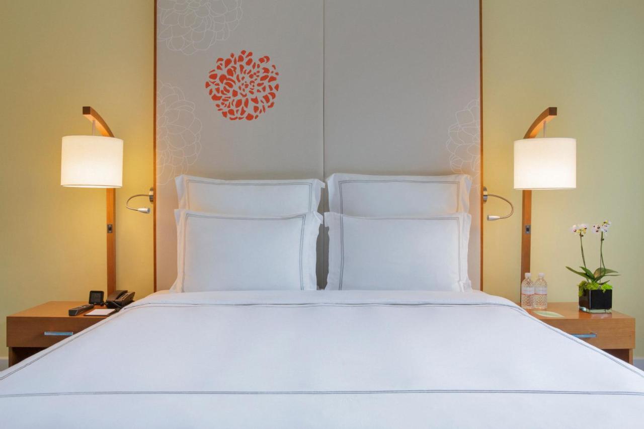 Paradox Singapore Merchant Court At Clarke Quay Екстер'єр фото The photo showcases a cozy hotel room with a neatly made bed featuring white linens and two pillows. Behind the bed is a decorative headboard with a simple floral design in orange. On either side of the bed, there are stylish bedside lamps providing 